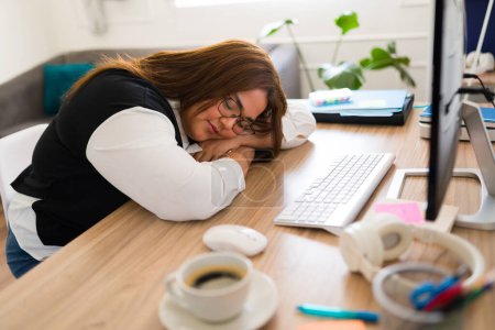 Foto de Mujer profesional cansada durmiendo en su escritorio frente a la computadora mientras trabaja en su oficina - Imagen libre de derechos