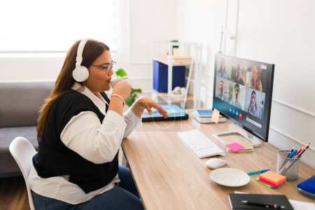 Foto de Atractiva mujer feliz bebiendo café en su oficina mientras hace una videollamada de negocios y trabaja en su escritorio - Imagen libre de derechos