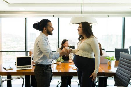 Businessman shaking hands with pregnant female colleague during a meeting in office board room