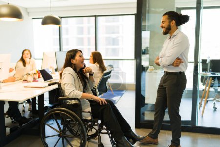 Photo for Disabled businesswoman sitting on wheelchair talking with male colleague standing by in office - Royalty Free Image