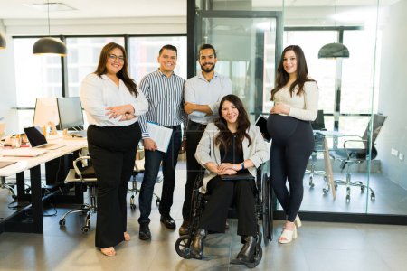 Téléchargez les photos : Portrait d'un groupe d'hommes d'affaires multiraciaux avec un gestionnaire handicapé assis en fauteuil roulant dans un bureau moderne - en image libre de droit
