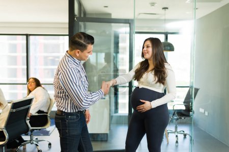 Téléchargez les photos : Homme d'affaires adulte moyen serrant la main d'une femme d'affaires enceinte dans un bureau - en image libre de droit