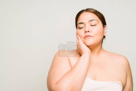 Foto de Relajada hermosa mujer grande con hombros desnudos haciendo su rutina de cuidado de la piel y sentirse amor propio aislado en el estudio - Imagen libre de derechos