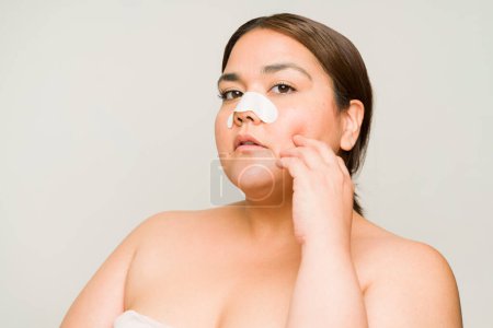 Photo for Plus size hispanic woman putting nose trips to remove blackheads while doing her skin care routine with bare shoulders - Royalty Free Image