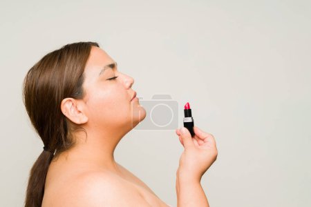 Foto de Mujer obesa en sus 30 usando lápiz labial y maquillaje producto de belleza con confianza en el amor propio aislado en un fondo de estudio - Imagen libre de derechos