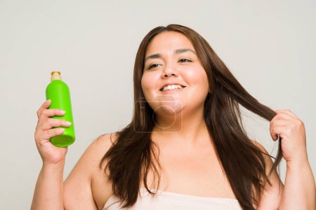 Photo for Plus size happy woman in her 30s smiling and using conditioner and taking care of her beautiful hair looking cheerful - Royalty Free Image