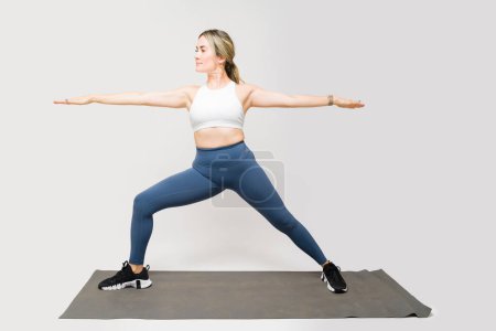 Téléchargez les photos : Belle femme en forme travaillant et faisant des exercices de posture de yoga guerrier sur un fond de studio blanc - en image libre de droit
