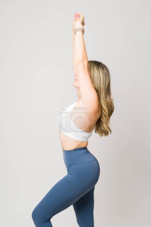 Téléchargez les photos : Profil d'une femme caucasienne fitness avec un beau corps et butin levant les bras et s'étirant avant de s'entraîner - en image libre de droit