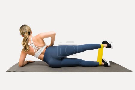 Photo for Rear view of an athletic fit girl with leggings working out using resistance bands and training on the exercise mat - Royalty Free Image