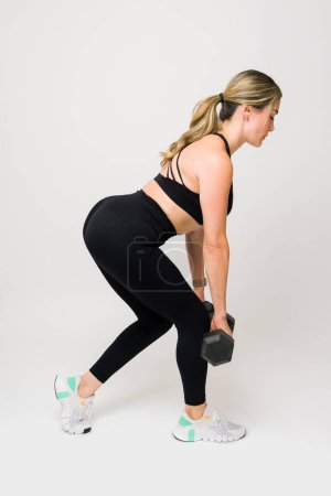 Photo for Caucasian fitness woman in her 30s doing deadlift training and lifting dumbbell weights in activewear against a white studio background - Royalty Free Image