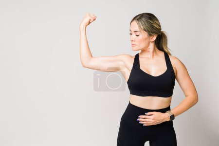 Foto de Atractiva mujer caucásica de unos 30 años con mucha fuerza haciendo un curl de bíceps y mostrando sus músculos después de hacer ejercicio - Imagen libre de derechos