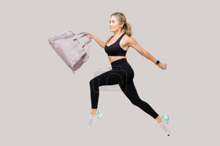 Téléchargez les photos : Femme en forme caucasienne rapide portant un sac de gym et courant tout en faisant de l'exercice et de l'exercice dans un fond de studio blanc - en image libre de droit