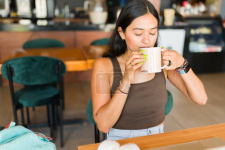 Téléchargez les photos : Attrayant jeune adulte et étudiant dans la vingtaine assis relaxant au café tout en buvant une tasse de café - en image libre de droit