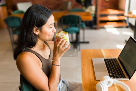 Téléchargez les photos : Belle femme faisant du travail à distance et buvant du café au café tout en tapant sur l'ordinateur portable étudiant - en image libre de droit