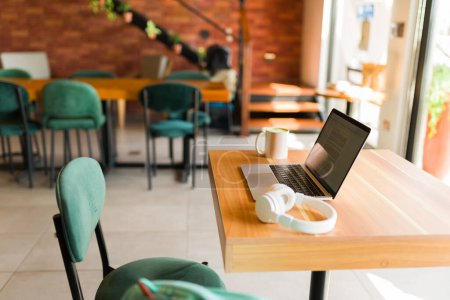 Téléchargez les photos : Magnifique café avec un ordinateur portable ouvert et écouteurs sur la table pour faire du travail à distance ou étudier avec la zone wifi - en image libre de droit