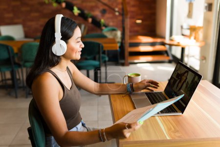 Téléchargez les photos : Femme heureuse avec écouteurs parler lors d'un appel vidéo et avoir un entretien d'embauche en utilisant Internet au café - en image libre de droit
