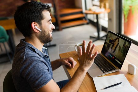 Téléchargez les photos : Homme joyeux entrepreneur et travailleur indépendant souriant tout en ayant un appel vidéo sur l'ordinateur portable dans le café - en image libre de droit