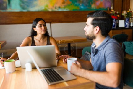 Téléchargez les photos : Attrayant homme et femme faisant travail indépendant ensemble comme un travail d'équipe en utilisant leurs ordinateurs portables et la zone wifi du café - en image libre de droit