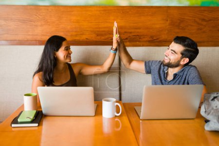 Téléchargez les photos : Couple excité de pigistes faire un high five et célébrer la fin de leur travail en équipe dans le café - en image libre de droit