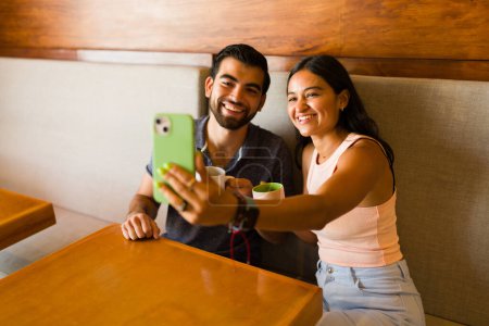 Foto de Hermosa pareja feliz tomando una selfie junto con un teléfono inteligente para las redes sociales durante una cita en una cafetería - Imagen libre de derechos