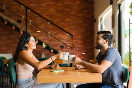 Téléchargez les photos : Couple latin heureux dans la vingtaine riant et s'amusant lors d'un rendez-vous café tout en se relaxant traîner dans un café - en image libre de droit