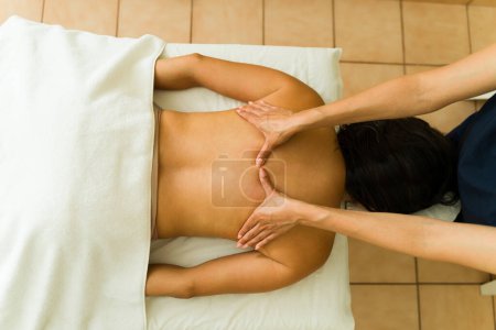 Foto de Mujer joven latina relajada en la mesa de masajes en el centro de spa de bienestar recibiendo un tratamiento relajante de un terapeuta - Imagen libre de derechos