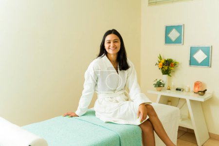 Photo for Portrait of a happy hispanic woman in her 20s smiling looking at the camera waiting for a massage at the beauty spa with a robe - Royalty Free Image
