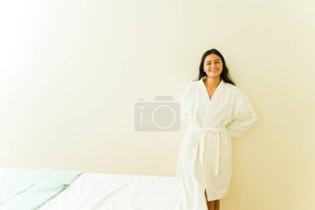 Photo for Happy young woman wearing a white robe looking relaxed  while preparing for a massage or beauty treatment at the spa - Royalty Free Image
