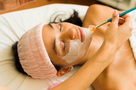 Téléchargez les photos : Attrayant jeune femme au spa de beauté obtenir un masque facial et un traitement de soins de la peau tout en se relaxant - en image libre de droit