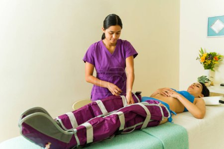 Téléchargez les photos : Thérapeute donnant pressothérapie à une cliente couchée et relaxante tout en recevant un traitement de massage - en image libre de droit