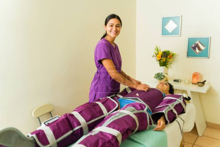 Téléchargez les photos : Joyeuse masseuse thérapeute souriante tout en travaillant au spa bien-être donnant massage pressothérapie - en image libre de droit