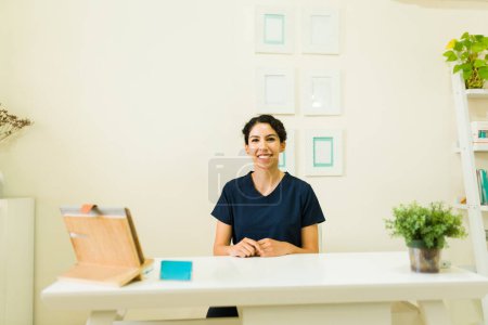 Photo for Happy attractive woman smiling while working as a desk receptionist for therapist at a beautiful beauty wellness spa - Royalty Free Image