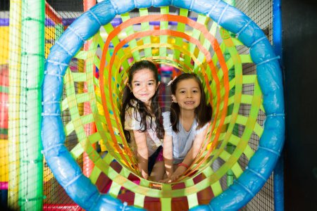 Foto de Retrato de linda niña amigos sonriendo y mirando feliz mientras juega en el túnel del patio de recreo y divertirse - Imagen libre de derechos