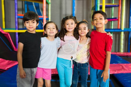 Foto de Adorables niños pequeños sonriendo mientras se ven felices en la sala de juegos cubierta y divertirse en el área de salto - Imagen libre de derechos