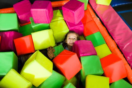 Téléchargez les photos : Petite fille drôle souriant tout en s'amusant à jouer à un jeu avec des cubes de mousse pendant les loisirs - en image libre de droit