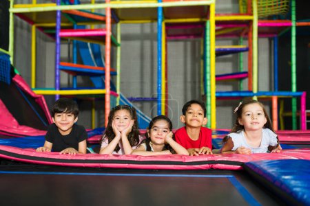 Téléchargez les photos : Heureux groupe d'enfants souriant tout en jouant avec des amis enfants dans la zone de trampoline de l'aire de jeux intérieure - en image libre de droit