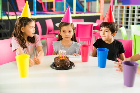 Foto de Adorables niños soplando las velas de cumpleaños mientras esperan el pastel y celebrando durante una fiesta de niños en el patio interior - Imagen libre de derechos