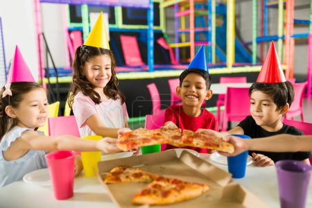 Foto de Feliz grupo de niños divirtiéndose celebrando una fiesta de cumpleaños con amigos mientras ríen y sonríen juntos en la sala de juegos cubierta - Imagen libre de derechos