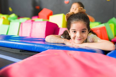 Foto de Linda adorable niña sonriendo en la sala de juegos mientras disfruta jugando en el área de trampolín utilizando cubos de espuma con sus amigos - Imagen libre de derechos