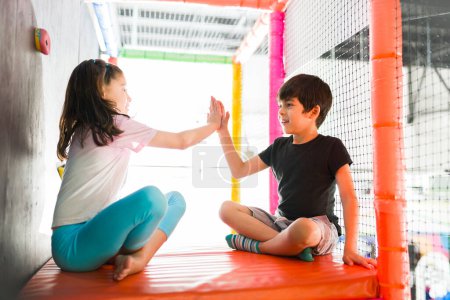 Téléchargez les photos : Enfants amusants faisant un high five dans la salle de jeux et souriant tout en jouant à un jeu et en s'amusant ensemble - en image libre de droit