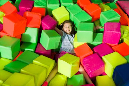 Foto de Divertido linda niña jugando un juego con cubos de espuma de colores y listo para el hoyo de la bola en el patio interior - Imagen libre de derechos