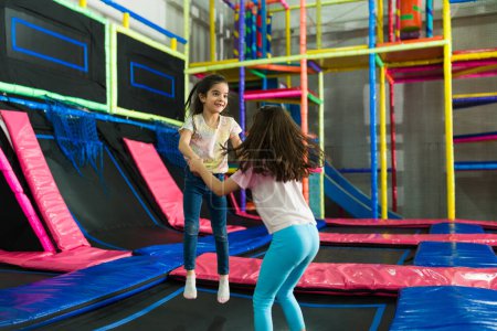 Emocionadas niñas saltando juntas tomadas de la mano y riendo mientras juegan con amigos en la zona de trampolín