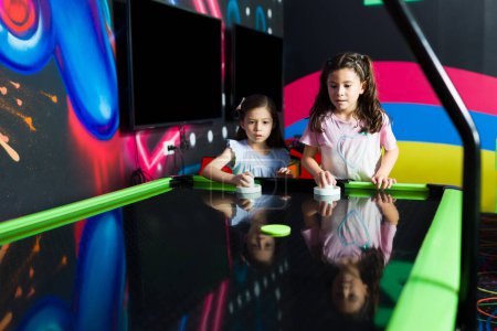 Photo for Beautiful young girls at the fun playground arcade playing air hockey together during a competition with friends - Royalty Free Image