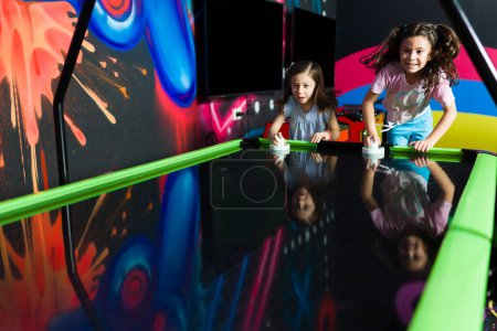 Photo for Excited children laughing and having fun while playing air hockey during a competition with friends in the arcade - Royalty Free Image