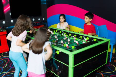 Foto de Alegre grupo de niños divirtiéndose en el arcade mientras juegan un juego de futbolín juntos en la sala de juegos cubierta - Imagen libre de derechos