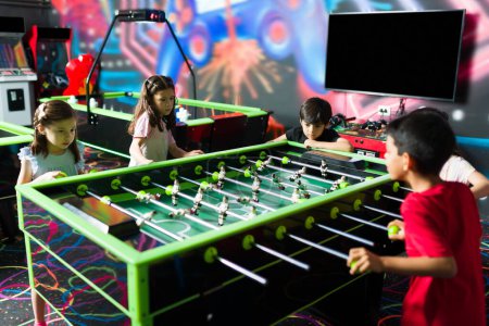 Photo for Happy group of kids at the arcade of the indoor playground  playing foosball during a fun competition  with friends - Royalty Free Image