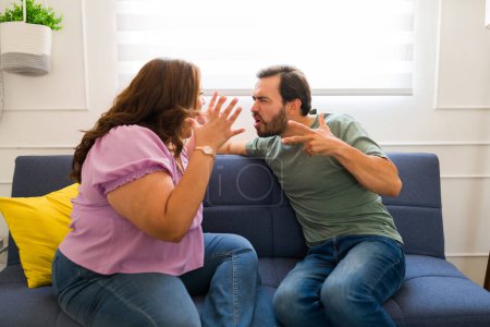 Téléchargez les photos : Couple furieux en colère criant et criant tout en se battant ou en se disputant à la maison à cause de problèmes relationnels - en image libre de droit