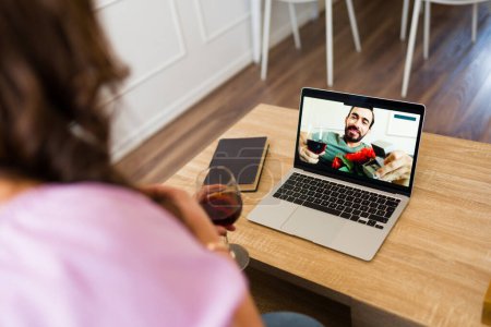 Photo for Girlfriend drinking wine seen from behind virtual dating and having a romantic long-distance relationship while talking on an online video call - Royalty Free Image