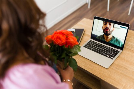 Téléchargez les photos : Femme romantique recevant des fleurs de son petit ami de longue distance souffler un baiser sur l'écran de l'ordinateur portable lors d'un appel vidéo - en image libre de droit