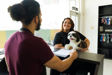 Téléchargez les photos : Homme travailleur vu de derrière parler de toilettage services avec un propriétaire de chien à la réception du spa pour animaux de compagnie - en image libre de droit